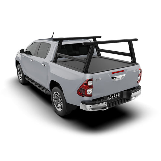 HSP Load Rack Pro fitted to white Toyota Hilux dual cab, angled rear view showing cross bars and a closed HSP Roller Cover