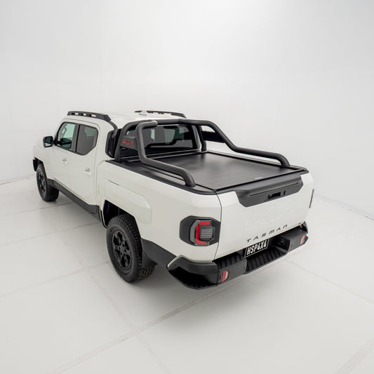 Angled 3/4 rear view of a white Kia Tasman fitted with an HSP Roll R electric roller cover in the closed position with black sports bars mounted.