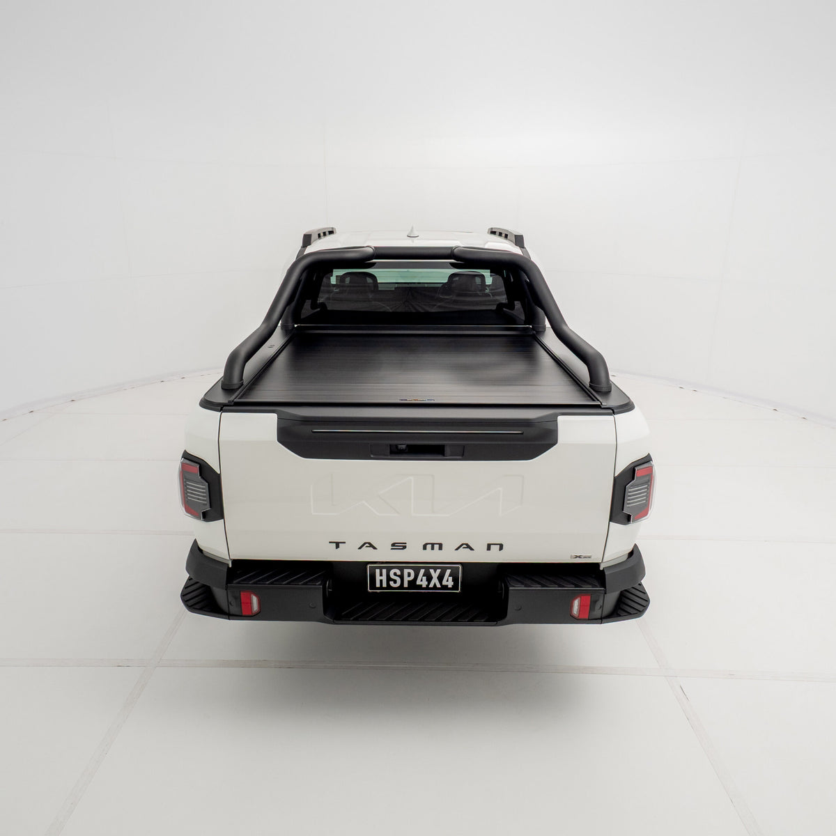 Straight rear view of a Kia Tasman fitted with the HSP Roll R electric roller cover, showing the closed aluminium roller shutter and integrated rear handle above the tailgate.