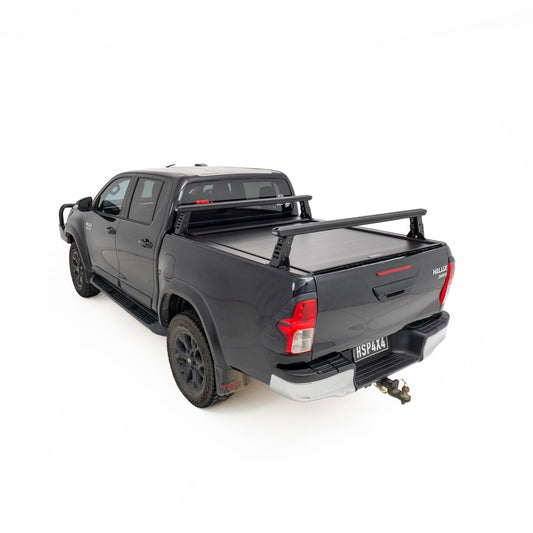 HSP Load Rack JNR fitted to black Toyota Hilux dual cab, rear three quarter view showing compact ladder rack over open tub fitted with a HSP Roller Cover